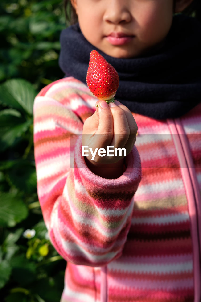 CLOSE-UP OF WOMAN HOLDING STRAWBERRY WHILE STANDING OUTDOORS