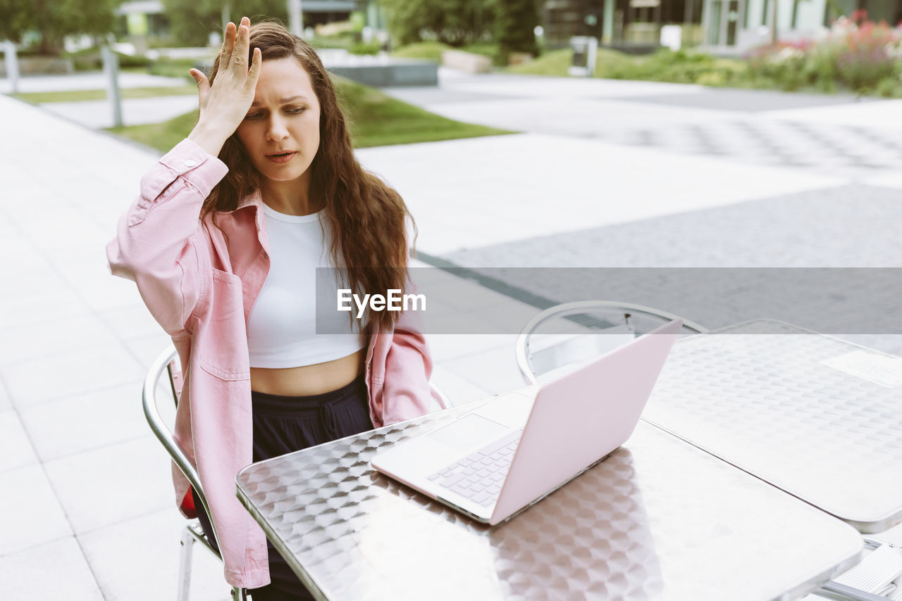 Young woman with laptop with facepalm gesture, feeling regret, sorrow, blaming herself for mistake