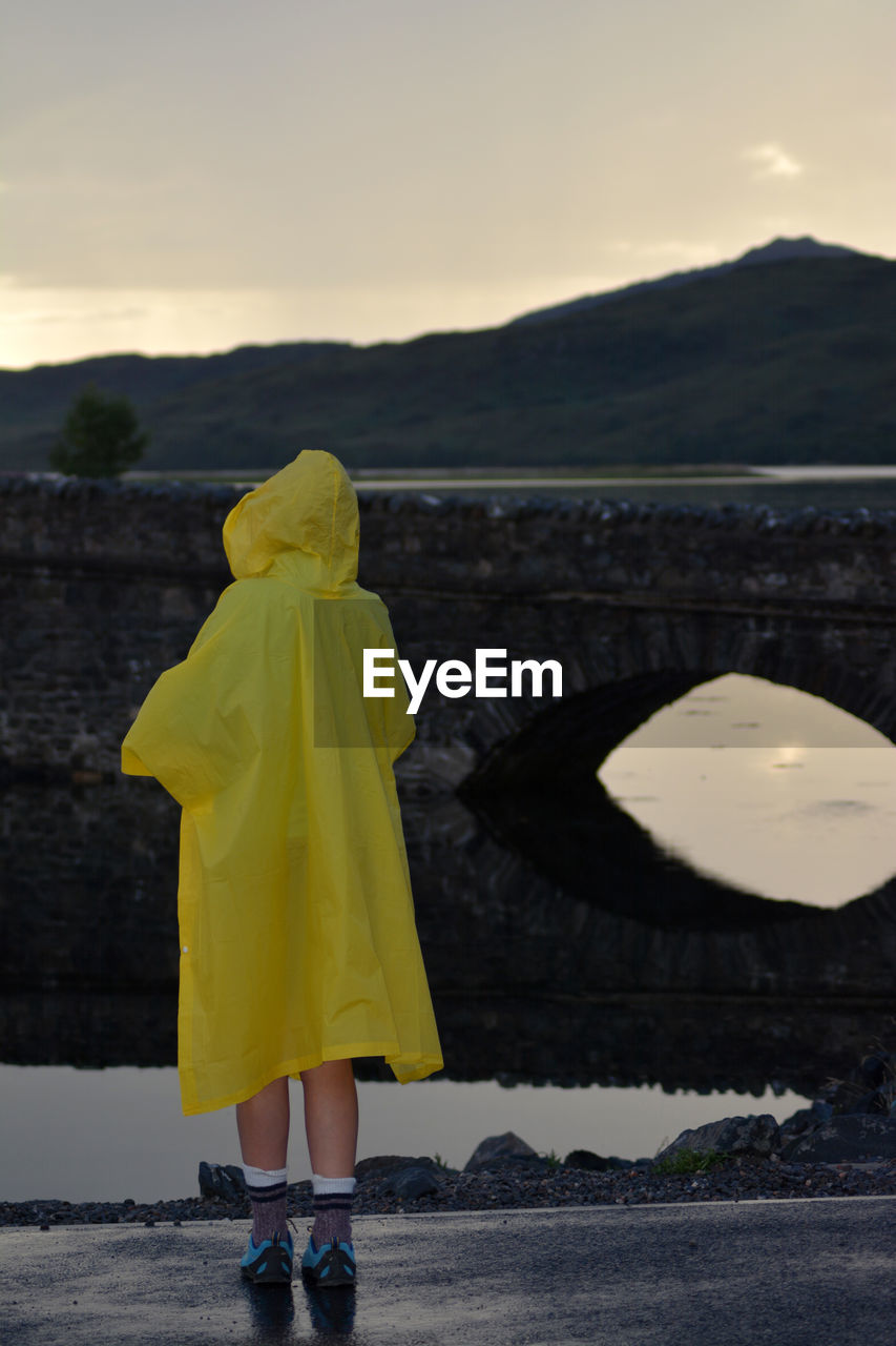 Rear view of woman standing at riverbank against sky