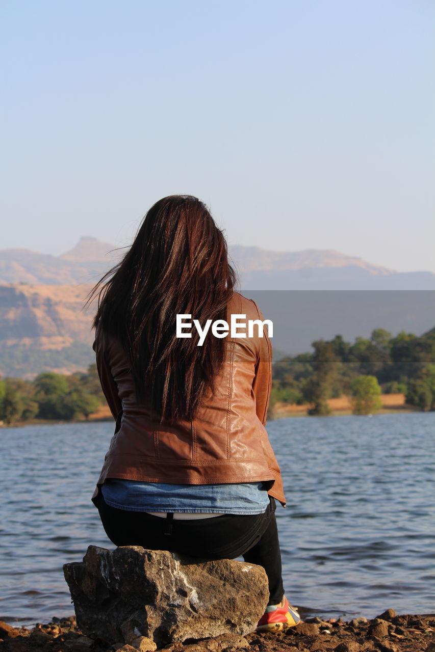 Rear view of woman sitting by lake against sky