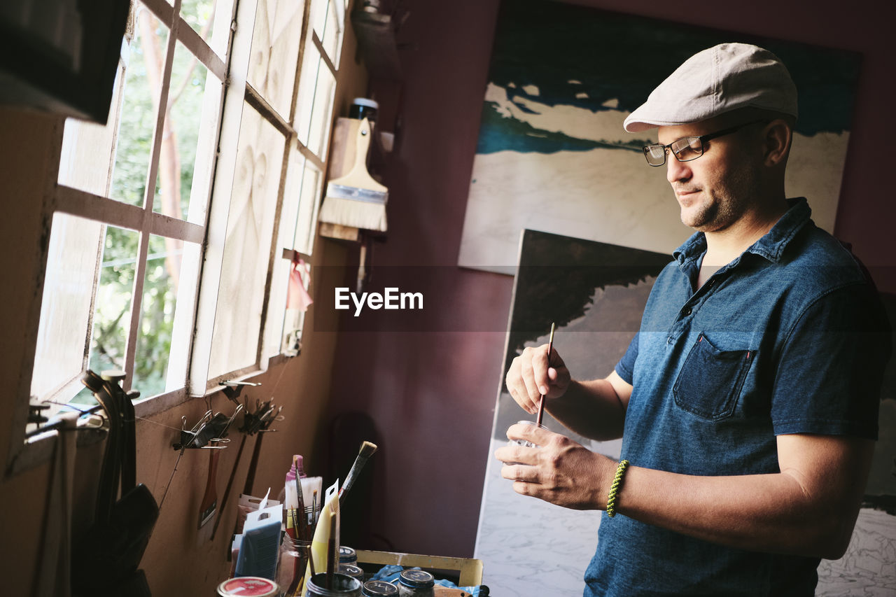 Mid adult male cuban artist mixing paint with brush in his workshop