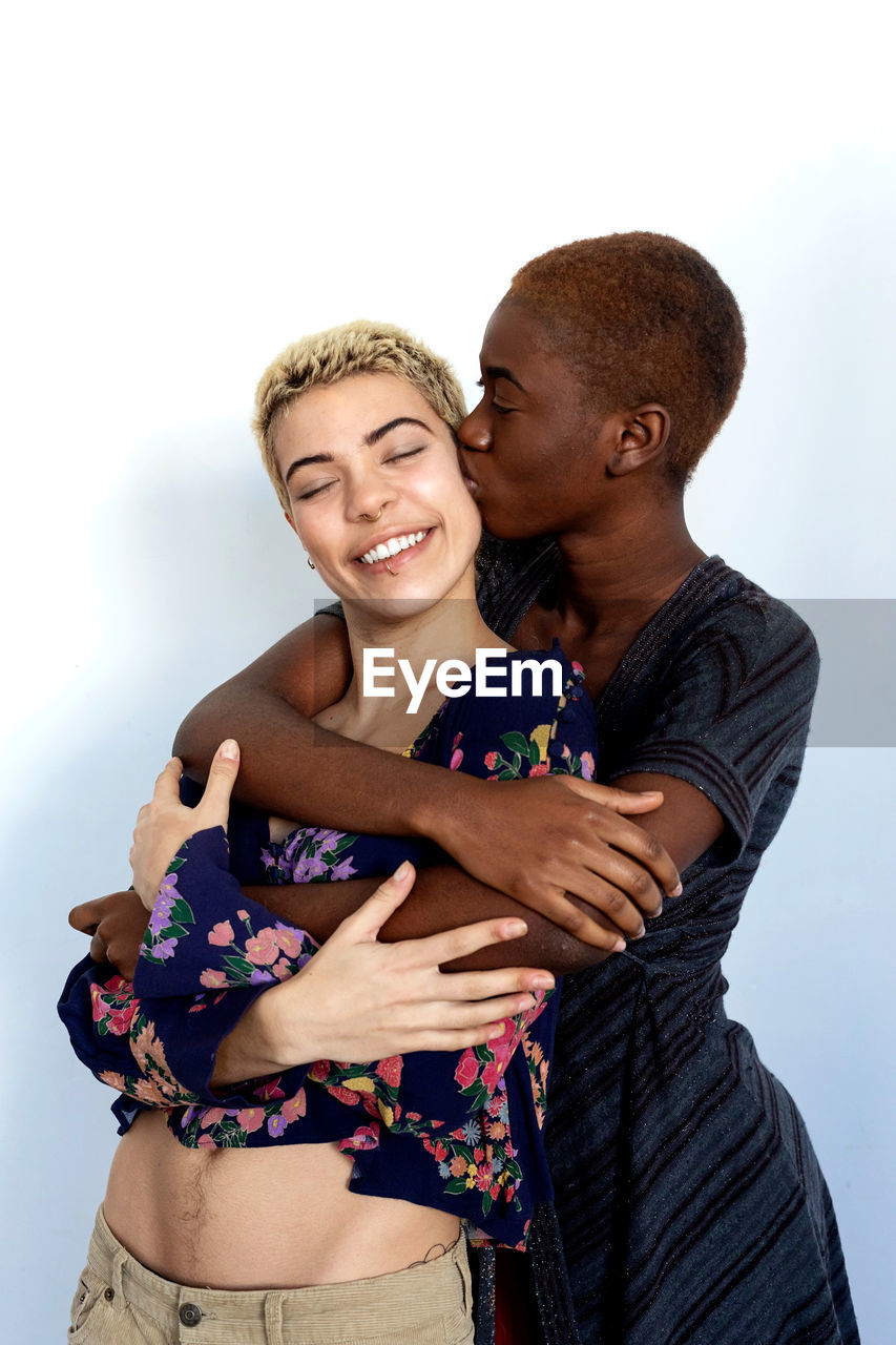 Portrait of smiling lesbian couple embracing against white background