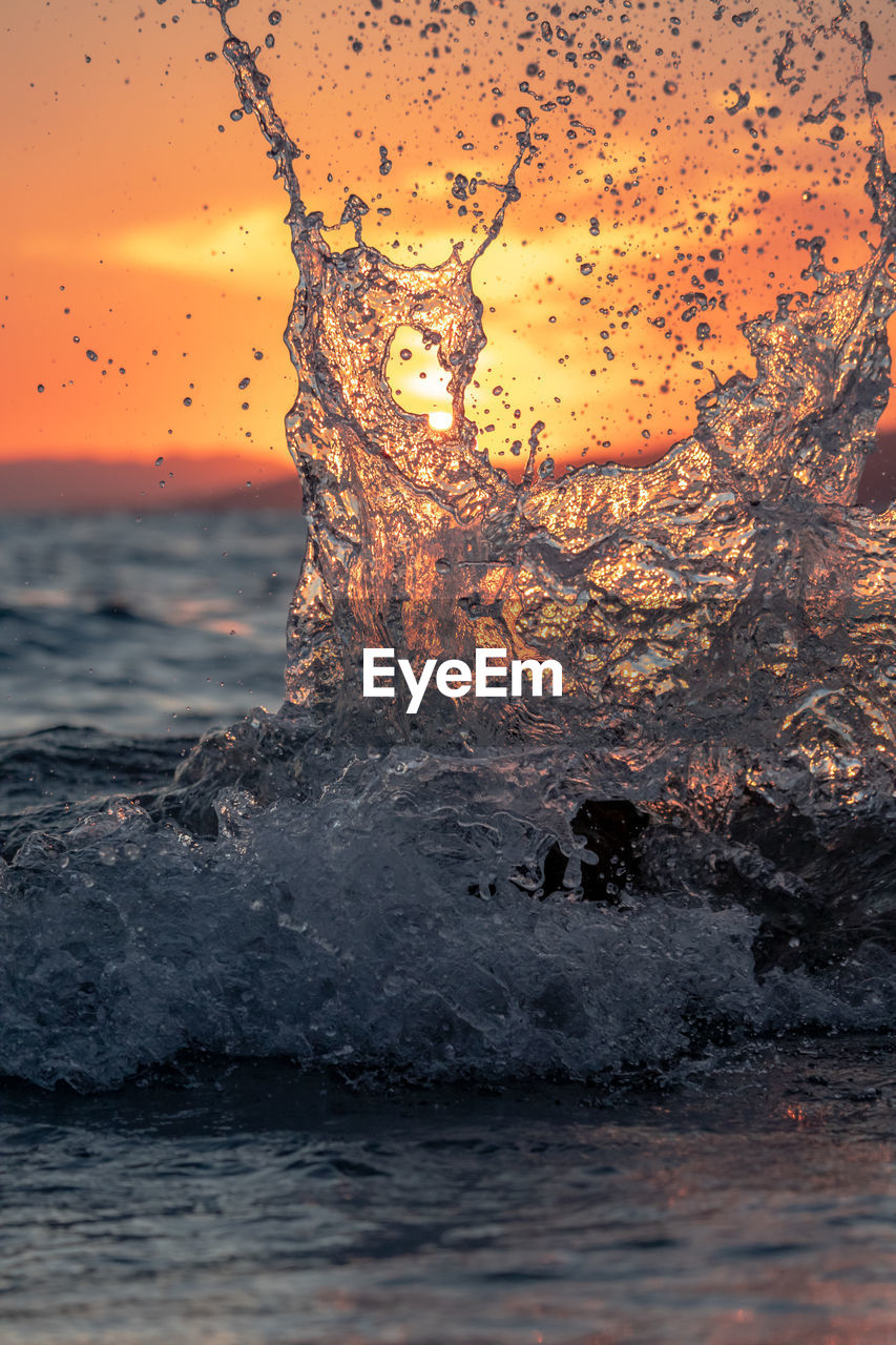 WATER SPLASHING IN SEA AGAINST ORANGE SKY