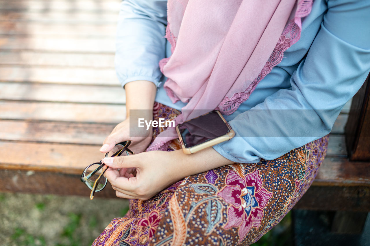 Midsection of woman wearing hijab with smart phone outdoors