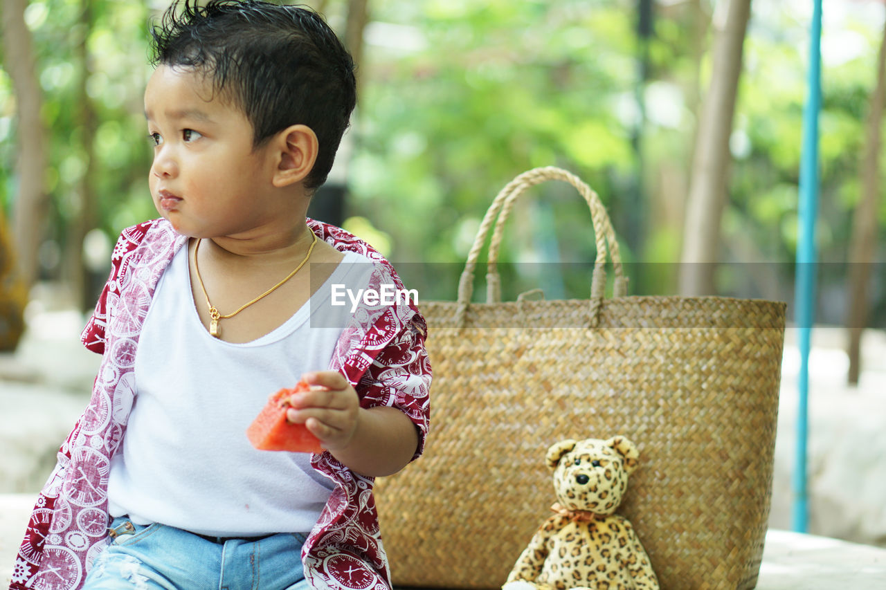 Cute baby boy looking away while eating fruit outdoor