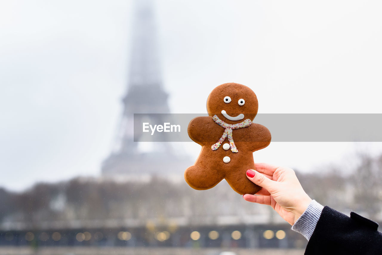 Cropped hand of woman holding gingerbread cookie against building