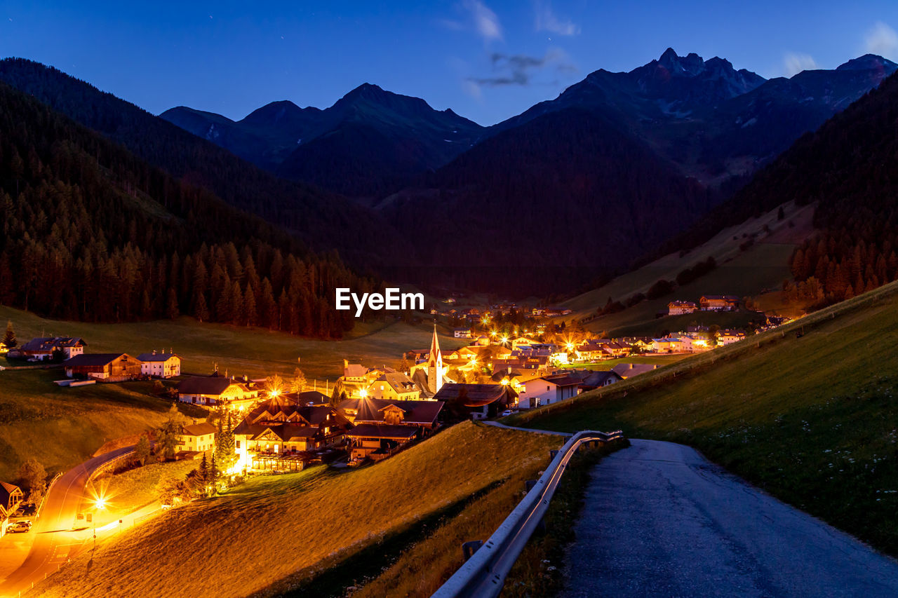 Road leading towards illuminated town against mountains