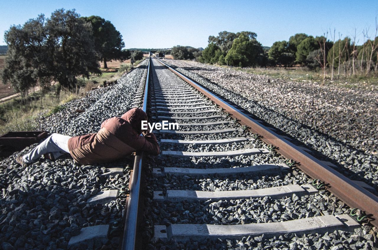Person relaxing on railroad track against sky