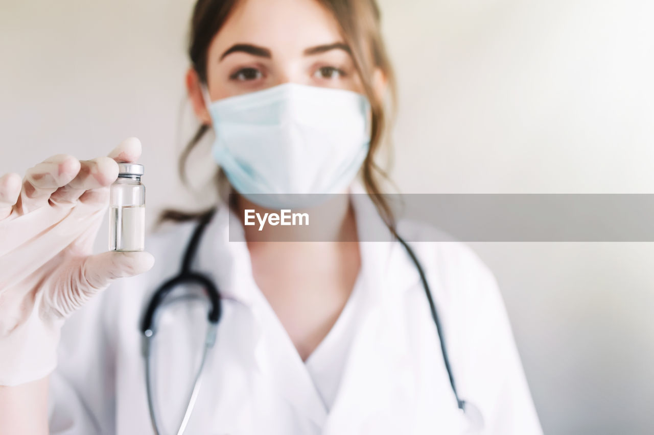 Woman doctor or nurse in lab, holding medicine liquid vaccine vial bottle preparing for injection