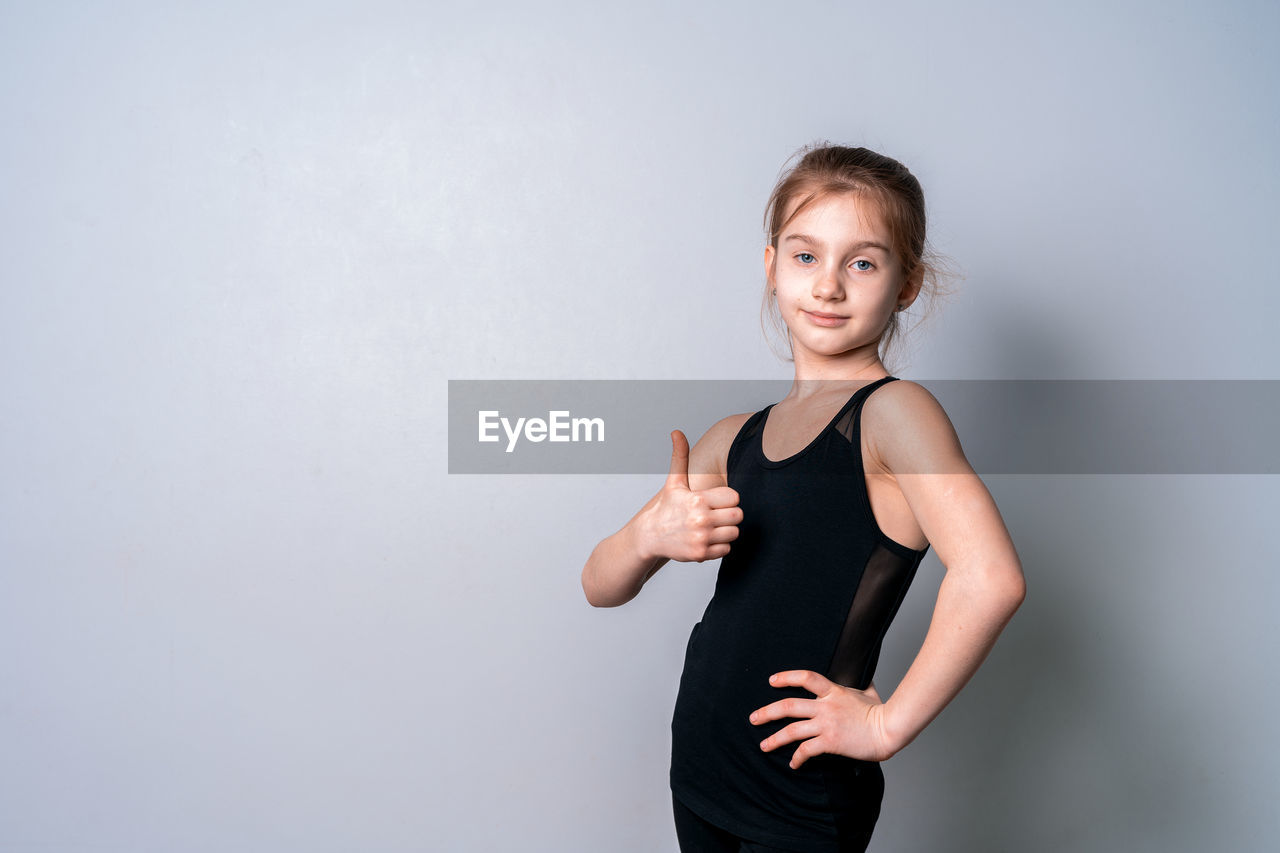 Portrait of girl showing thumbs up while standing against wall