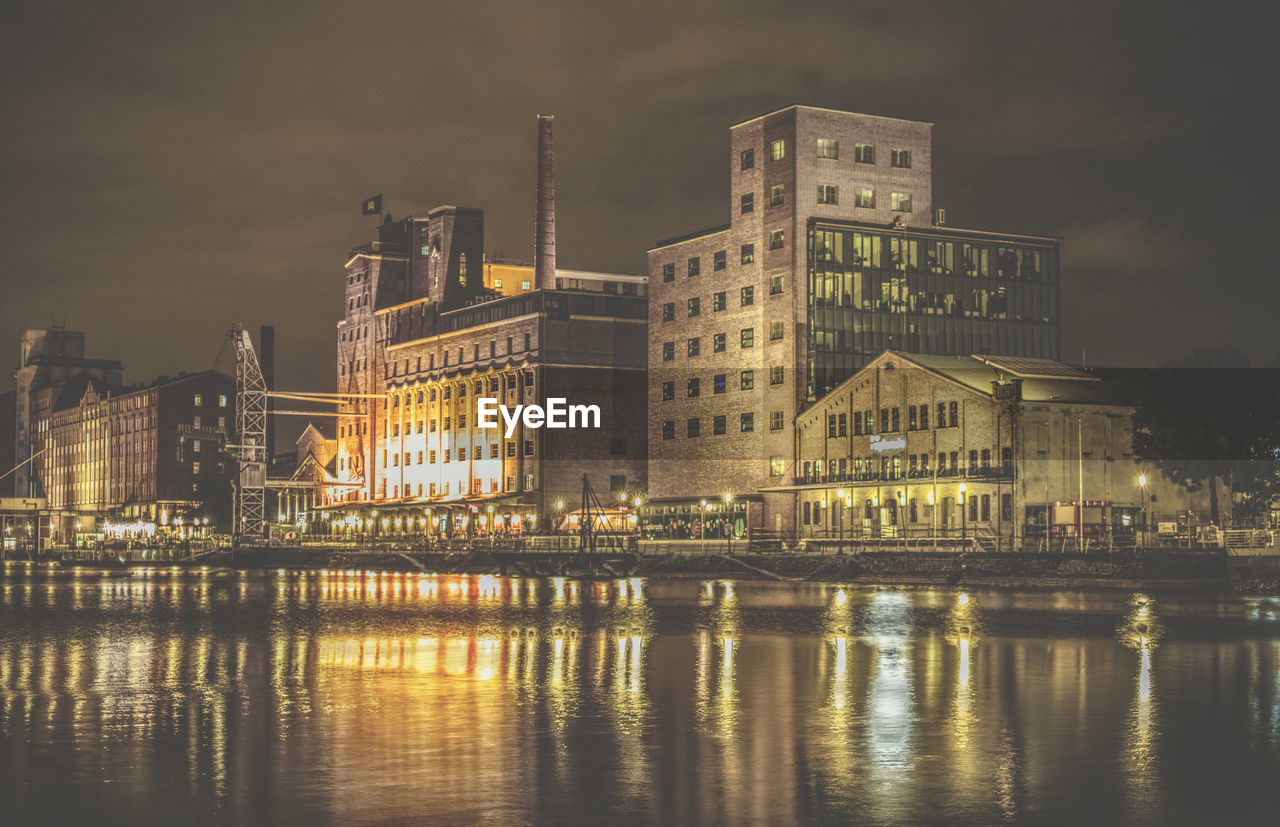 Illuminated buildings by river against sky in city at night