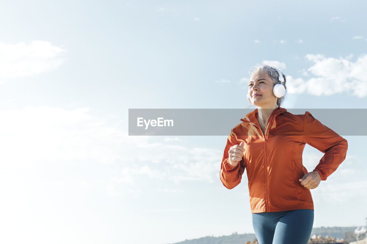 Mature woman listening to music through headphones and jogging on sunny day