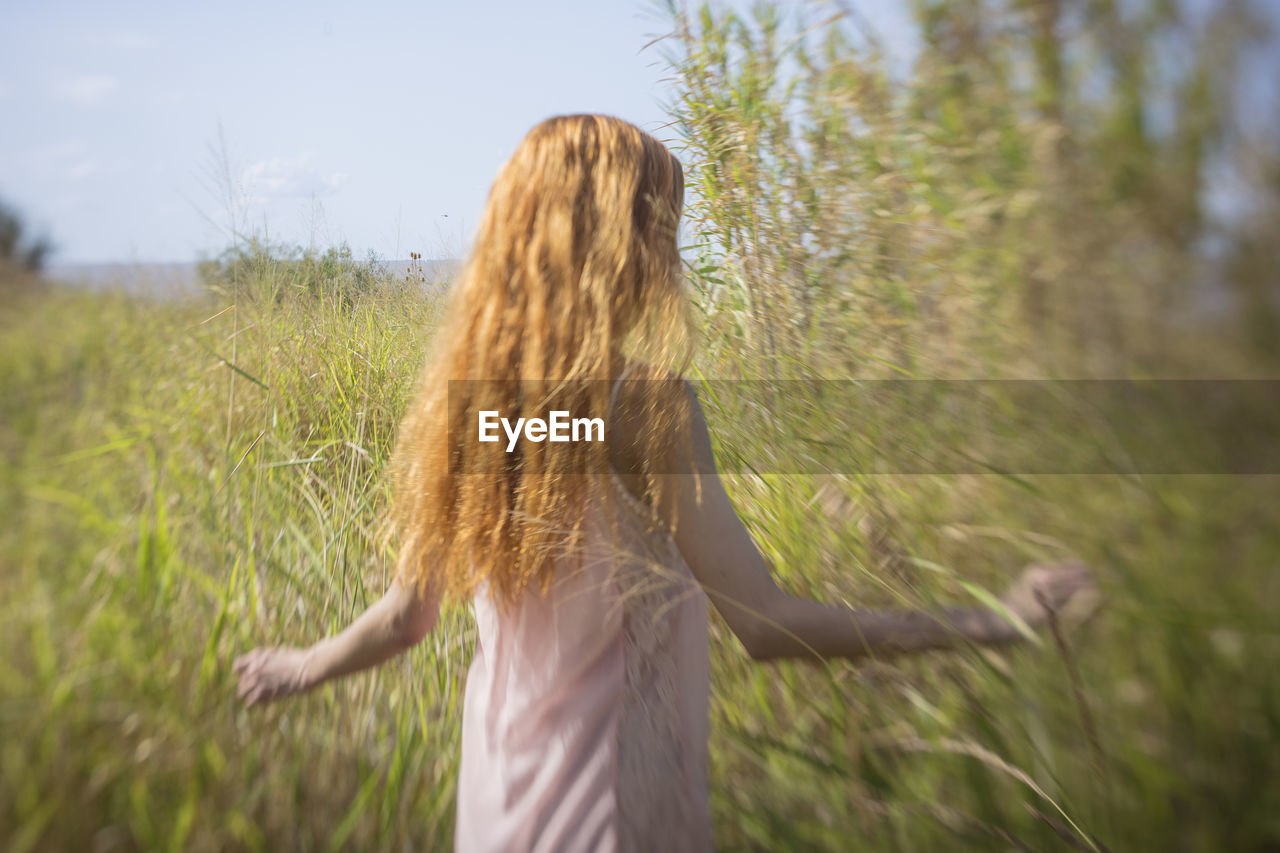 REAR VIEW OF WOMAN WITH ARMS RAISED ON FIELD