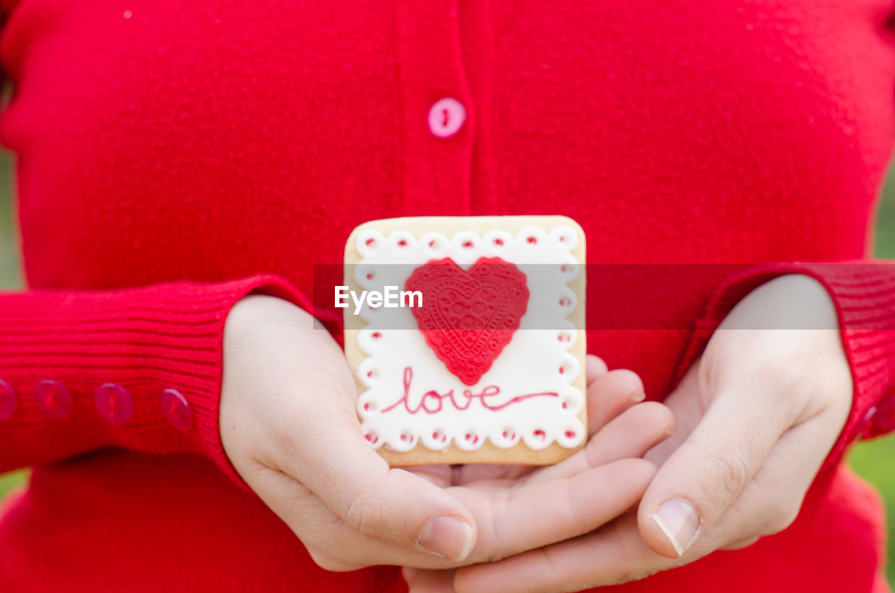 CLOSE-UP OF WOMAN HOLDING HEART SHAPE ON RED