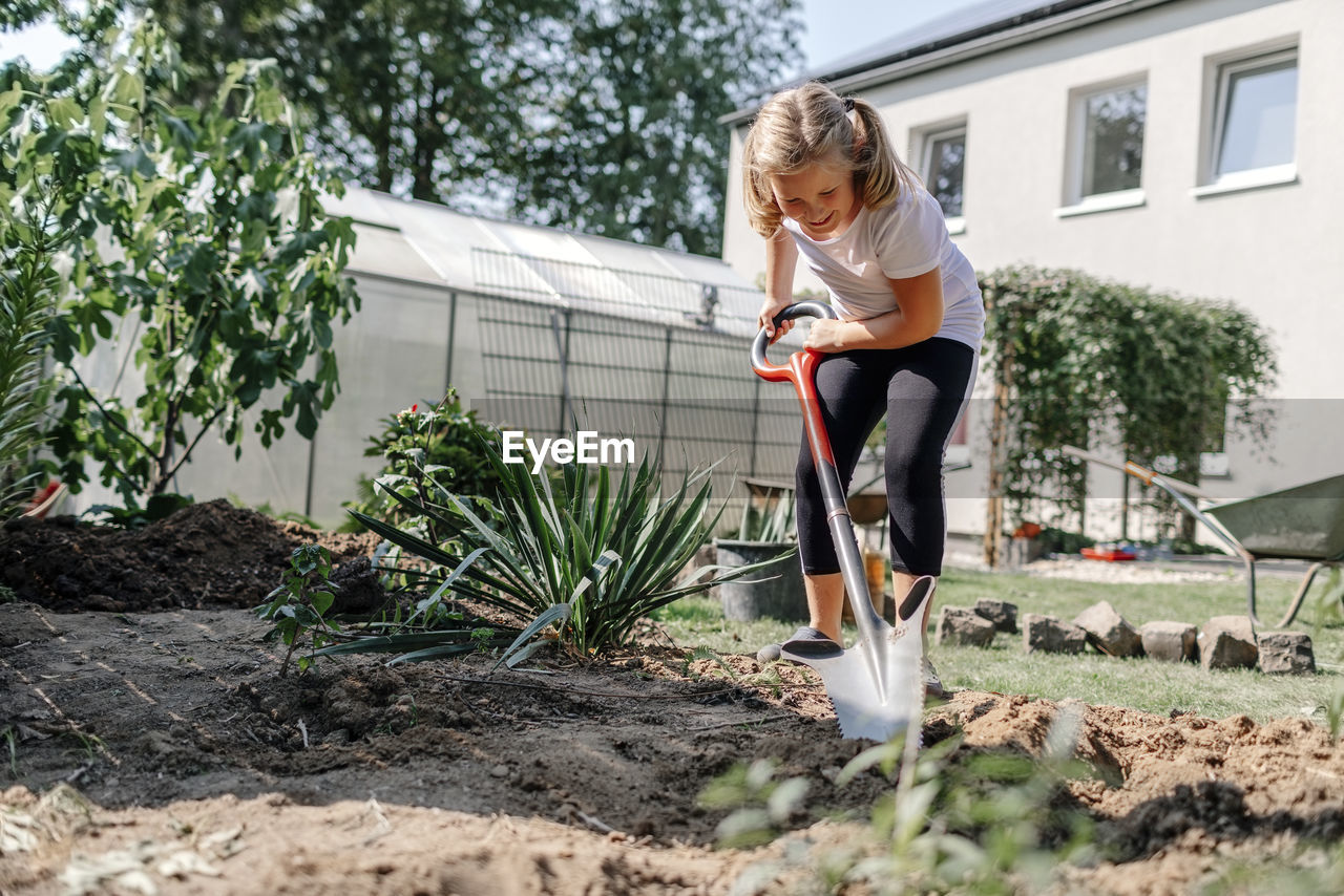 Smiling girl with shovel gardening in backyard