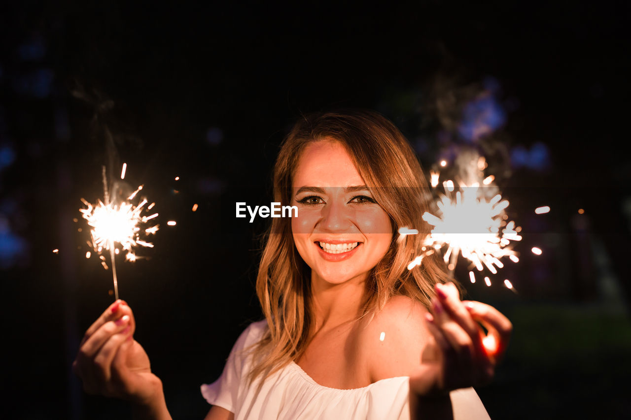 Portrait of smiling woman with fire crackers at night