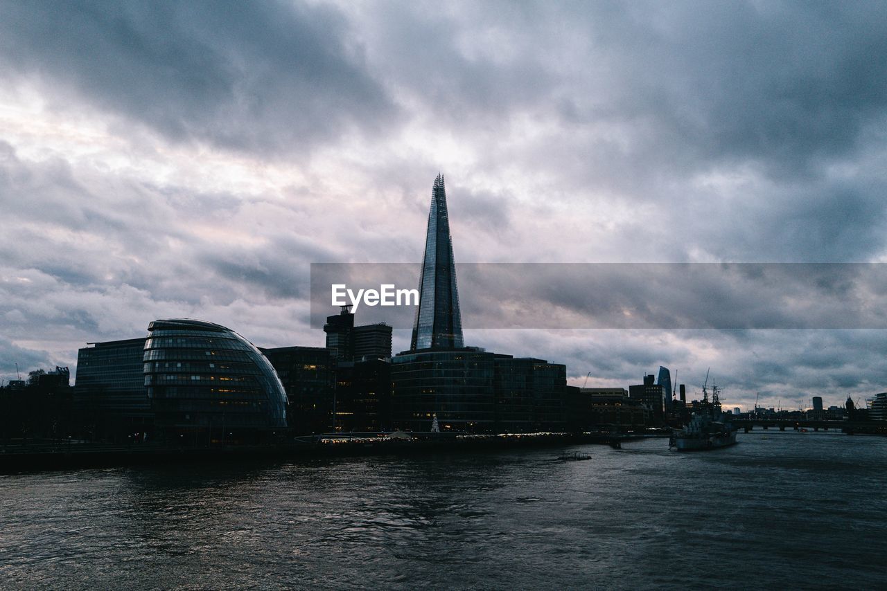 Buildings at waterfront against cloudy sky