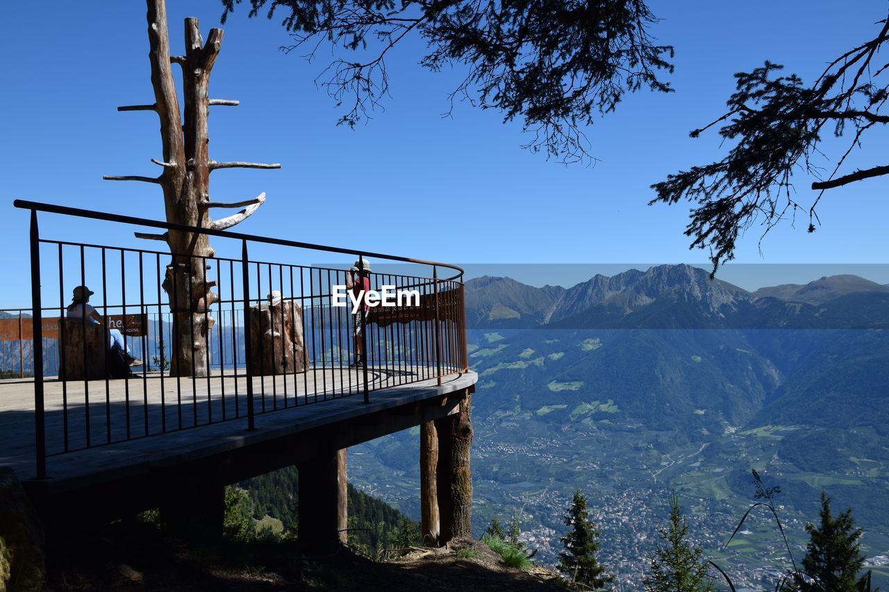 People at observation point by mountains against clear blue sky