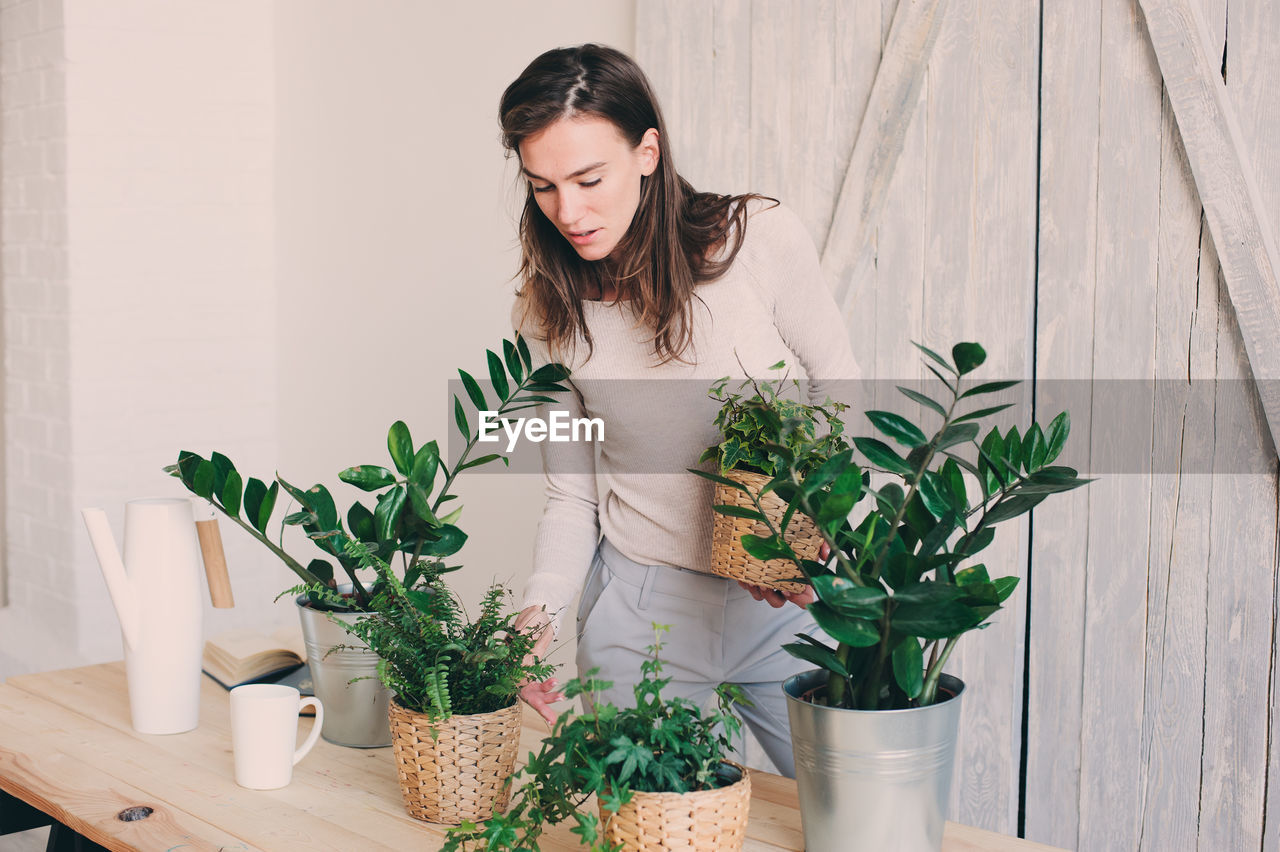 Young woman standing by potted plants on table at home