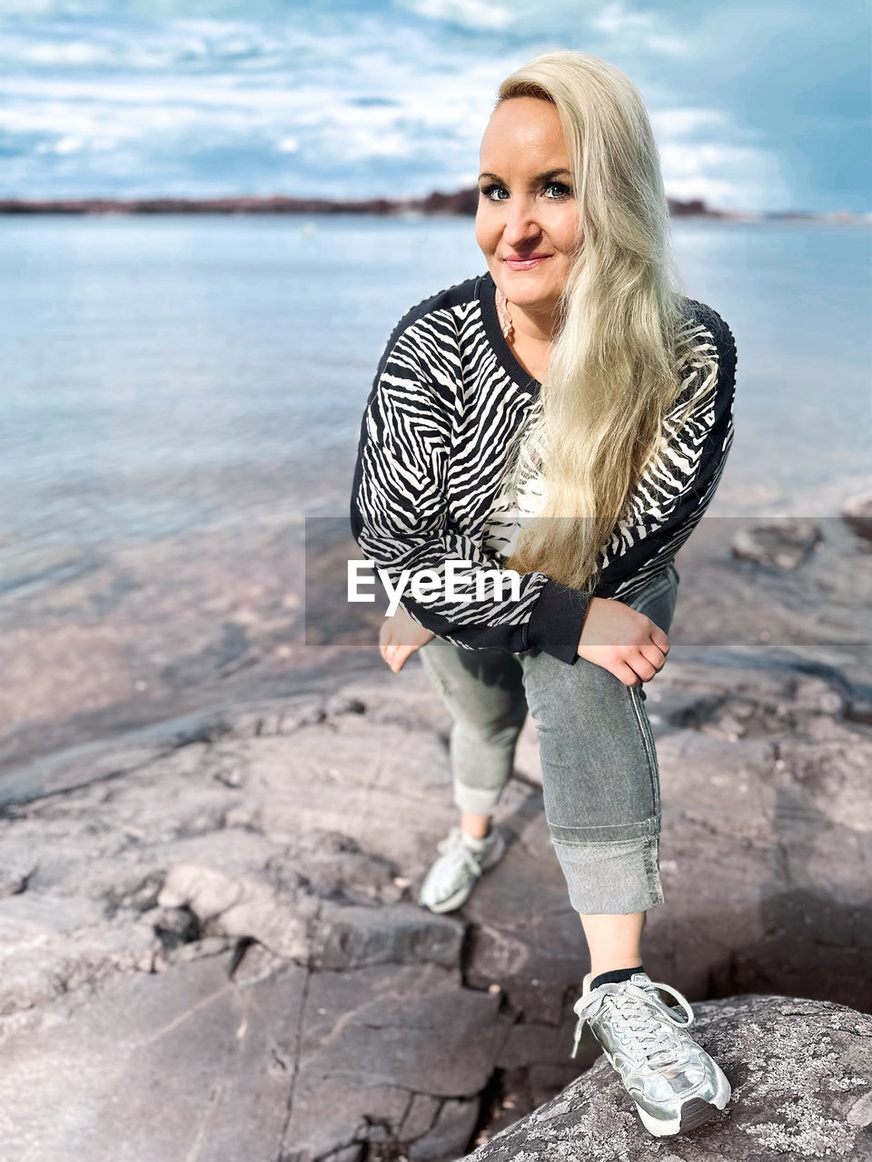 blond hair, one person, adult, women, water, beach, smiling, sea, portrait, spring, nature, casual clothing, hairstyle, fashion, full length, land, photo shoot, young adult, happiness, clothing, portrait photography, long hair, leisure activity, looking at camera, emotion, standing, female, rock, person, day, footwear, smile, sky, teeth, striped, lifestyles, outdoors, blue, human leg, front view, beauty in nature, trip, dress, holiday, looking, vacation, relaxation, cheerful