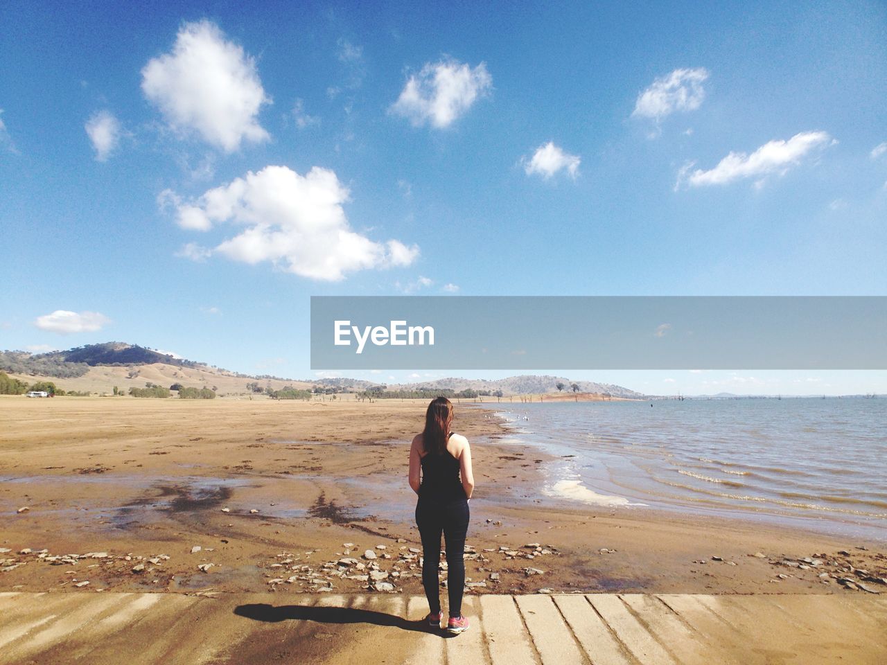 Rear view of woman standing at beach against sky