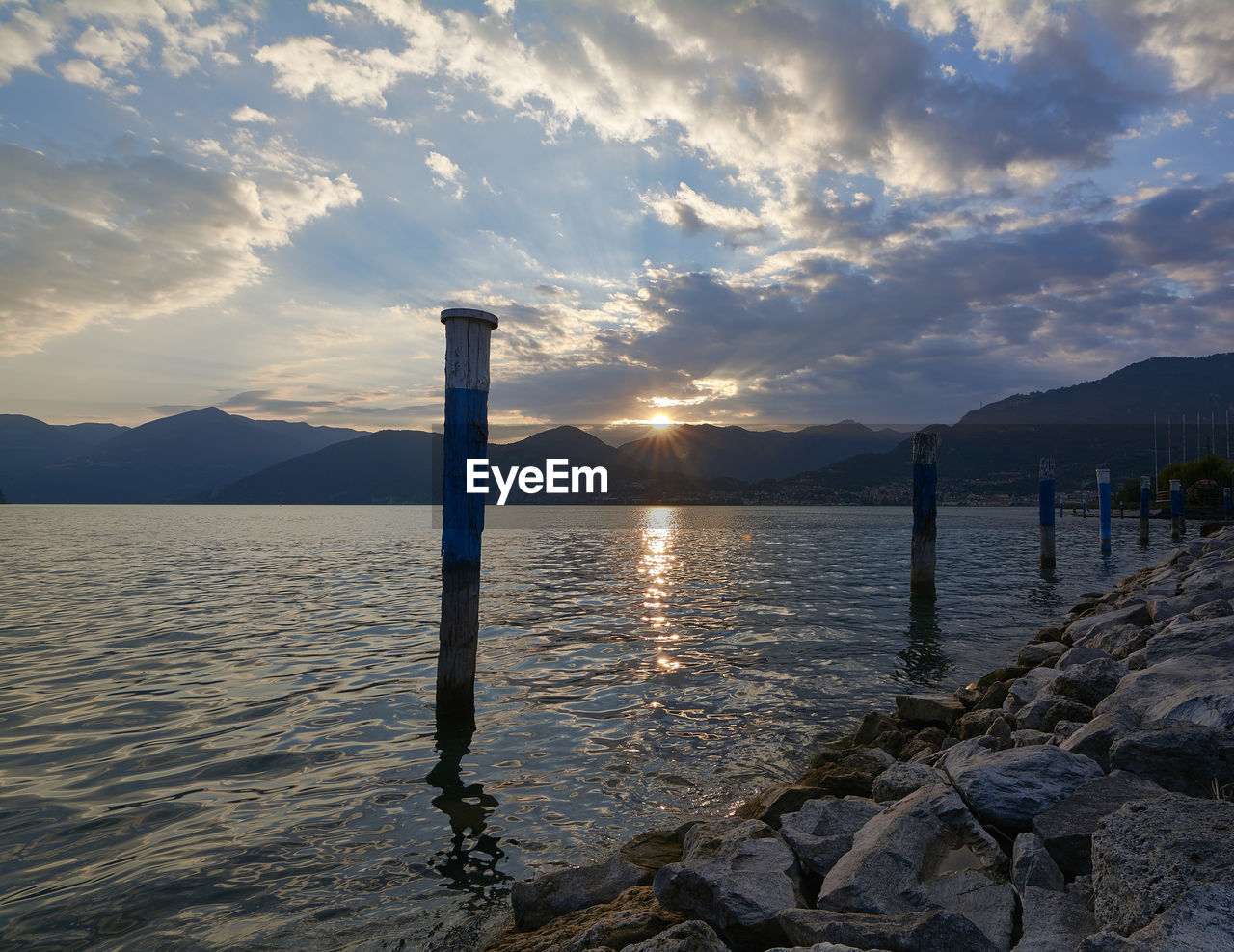 Wooden posts in river against cloudy sky