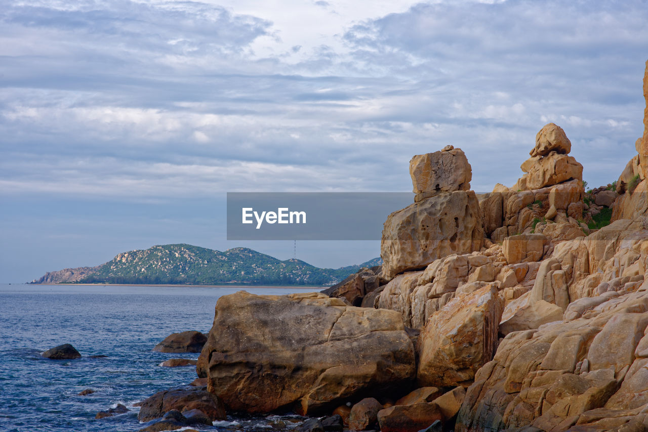 Rock formation by sea against cloudy sky