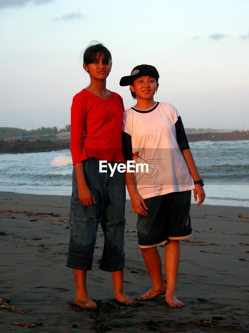 FULL LENGTH OF BOYS STANDING ON BEACH AGAINST SKY