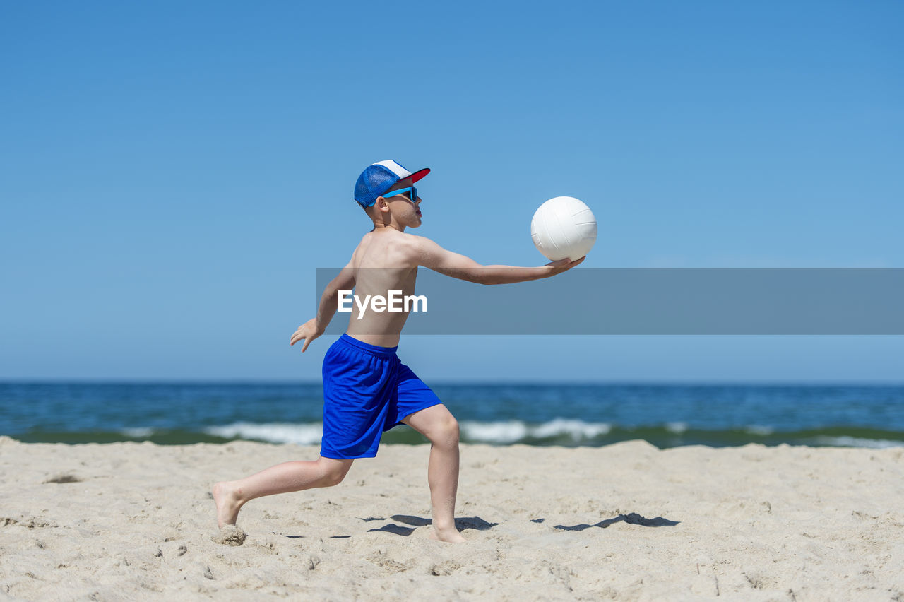 Boy playing volleyball against sea