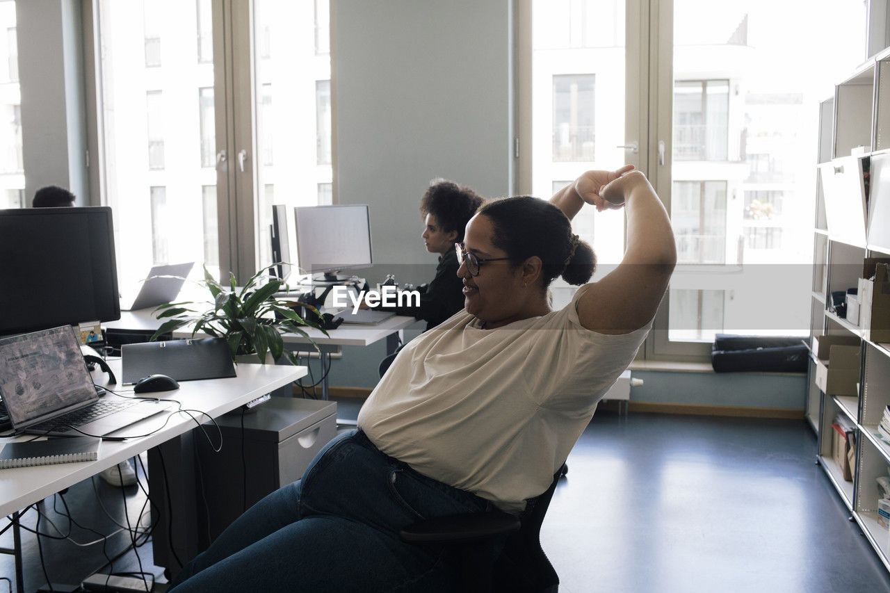 Female business professional stretching while sitting on chair at office