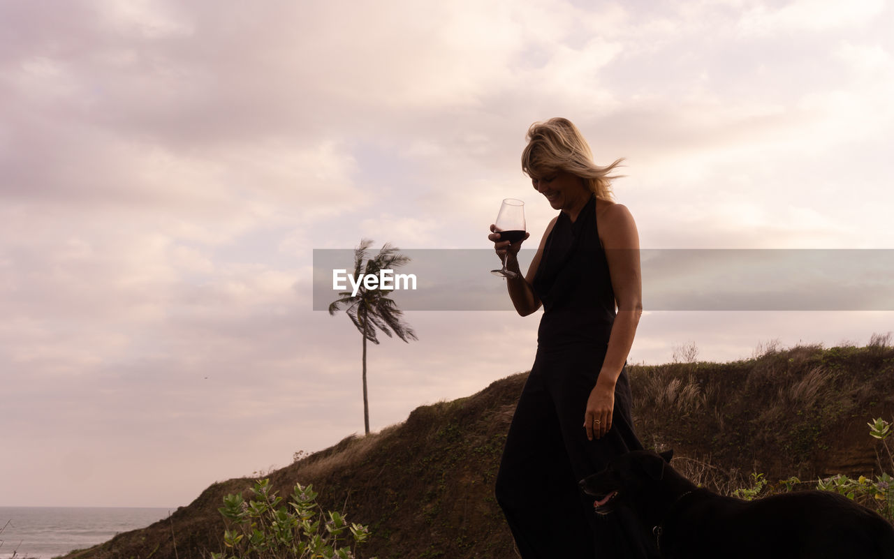 Woman drinking wine while standing on land against sky