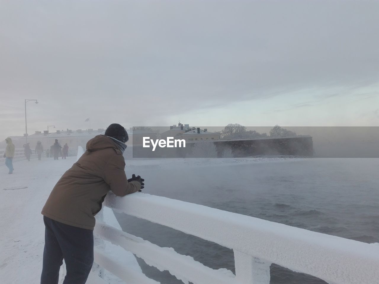 Man standing at snow covered shore against sky