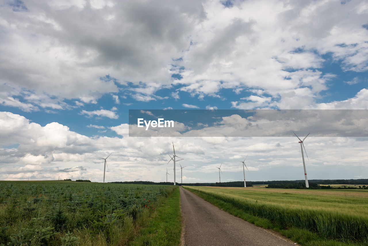 Street amidst wind turbines against cloudy sky