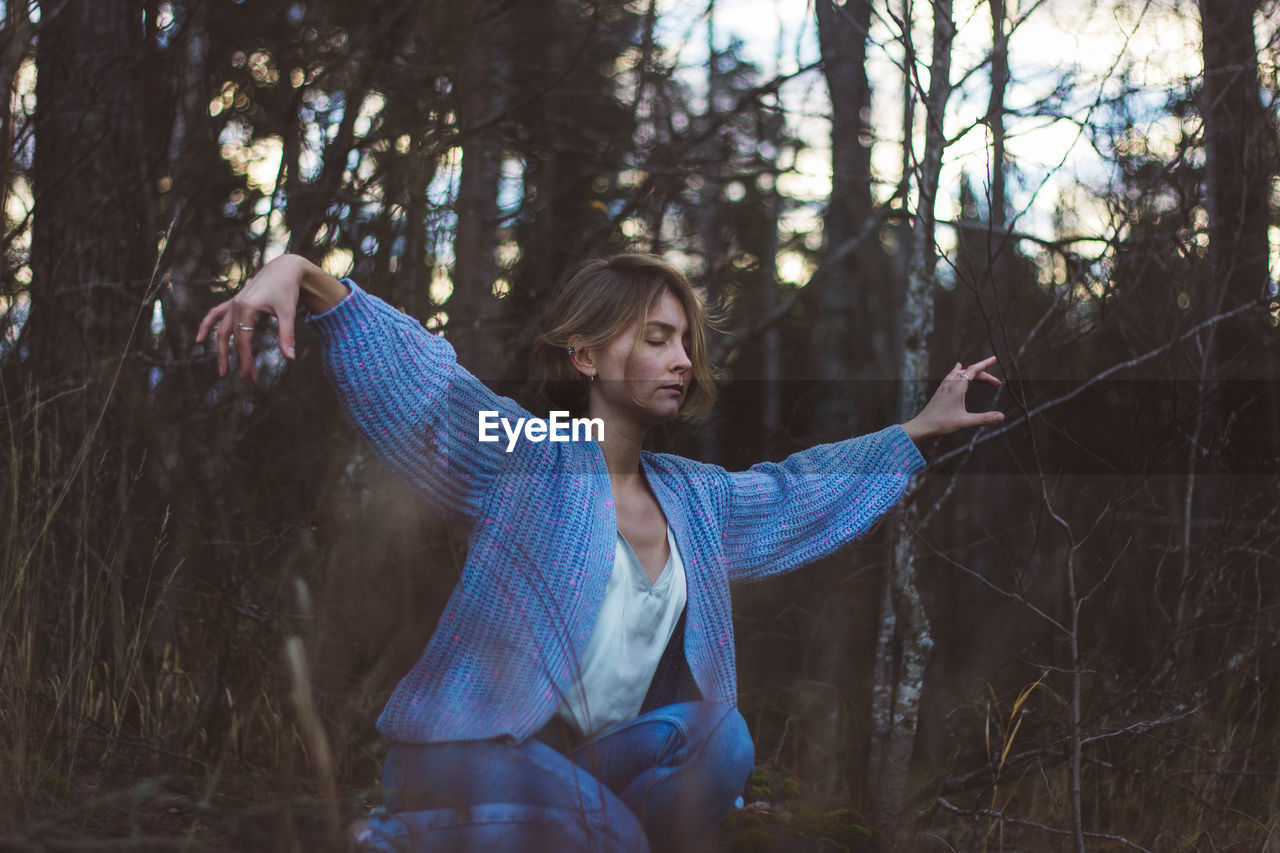 Young woman with eyes closed dancing against trees in forest