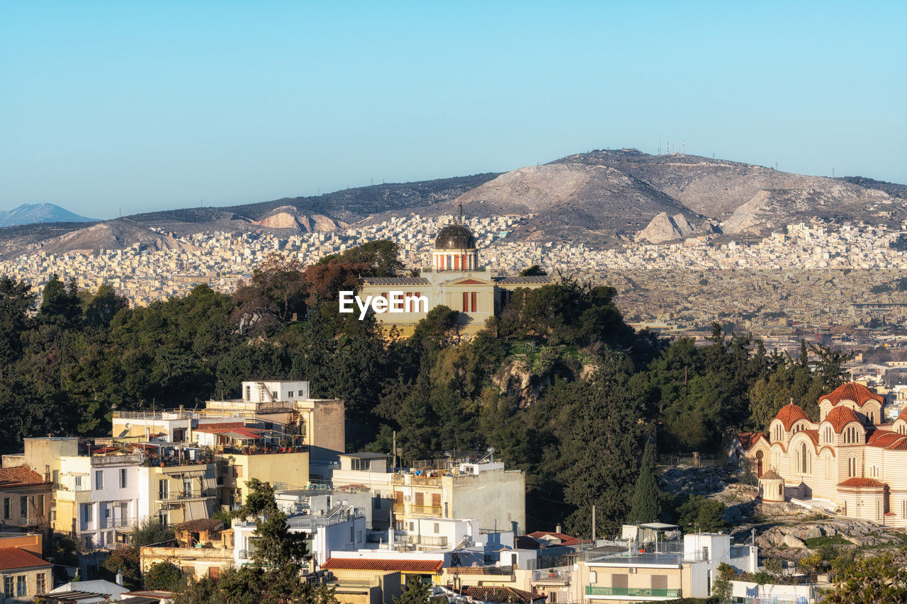 architecture, town, building exterior, built structure, building, mountain, city, tree, residential district, nature, village, house, plant, vacation, sky, clear sky, cityscape, no people, high angle view, travel destinations, mountain range, aerial photography, day, land, community, outdoors, travel, tourism, sunny, ancient history, blue, roof, sunlight, landscape, religion, sea, townscape, history, the past, scenics - nature