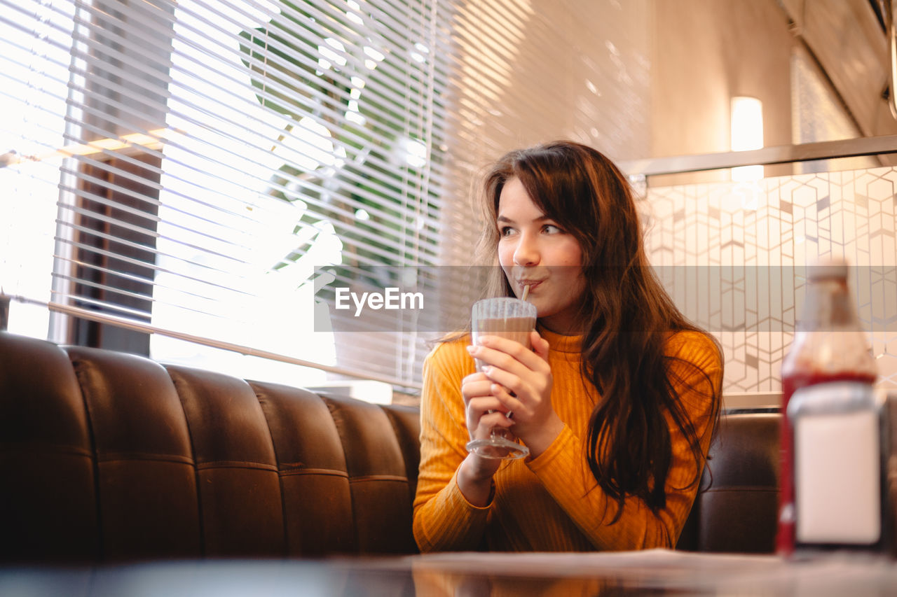 Teenage girl drinking chocolate milkshake in restaurant