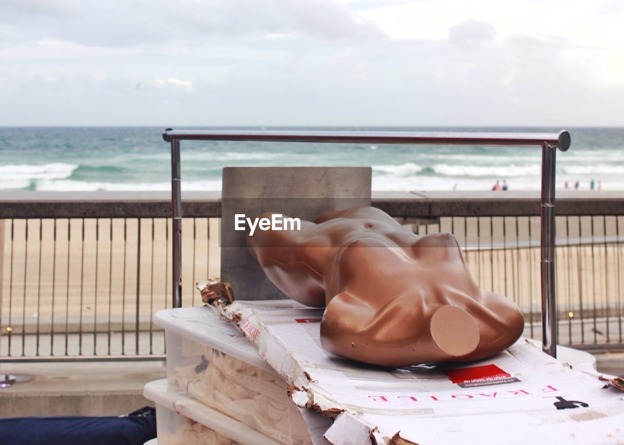 Abandoned mannequin on cardboard at beach against sky