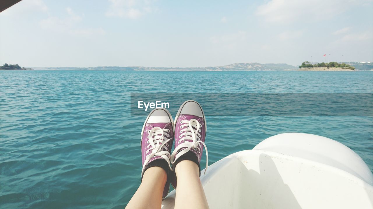 Close-up of feet with sport shoes against sea