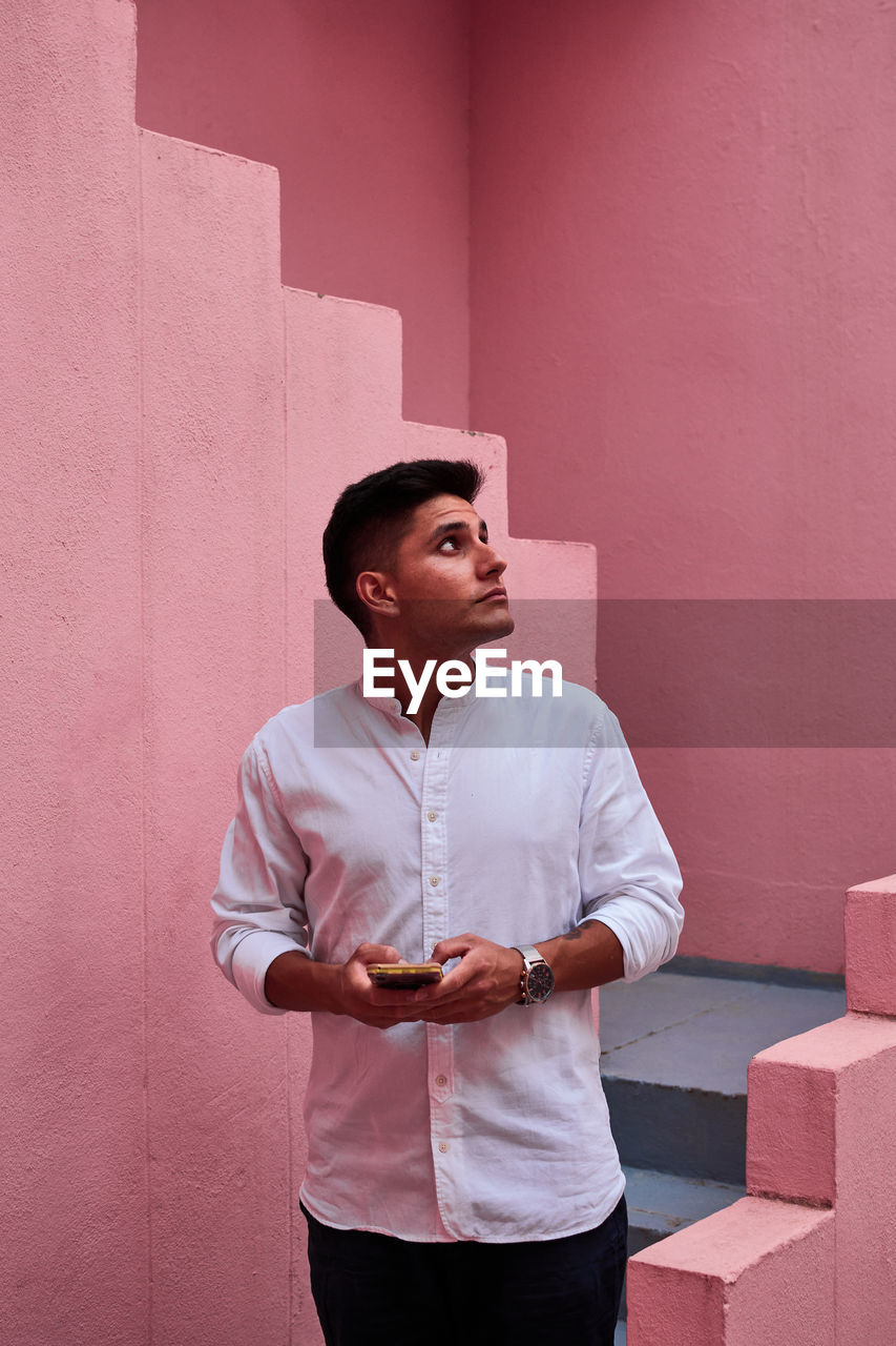 Young latin man holds his cell phone in a pink building