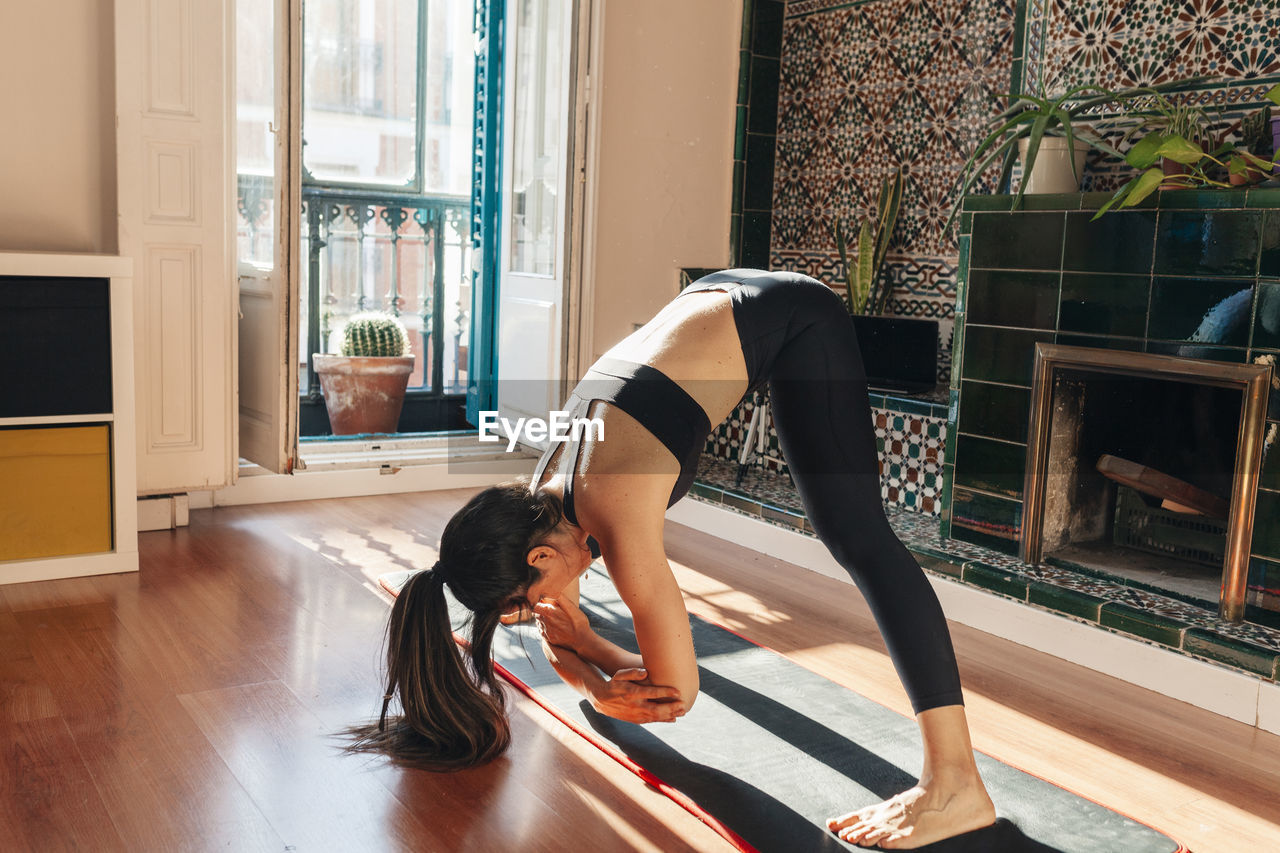 Young active woman stretching legs while practicing yoga at home