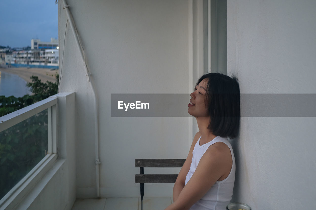 side view of young woman looking through window at home