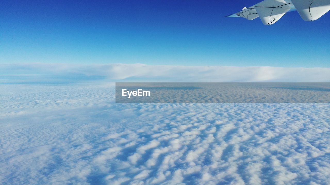 Cropped image of airplane flying over clouds against blue sky