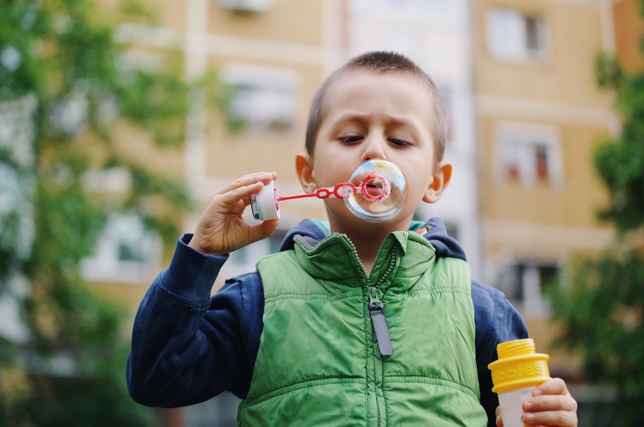 Close-up of boy blowing bubble against building