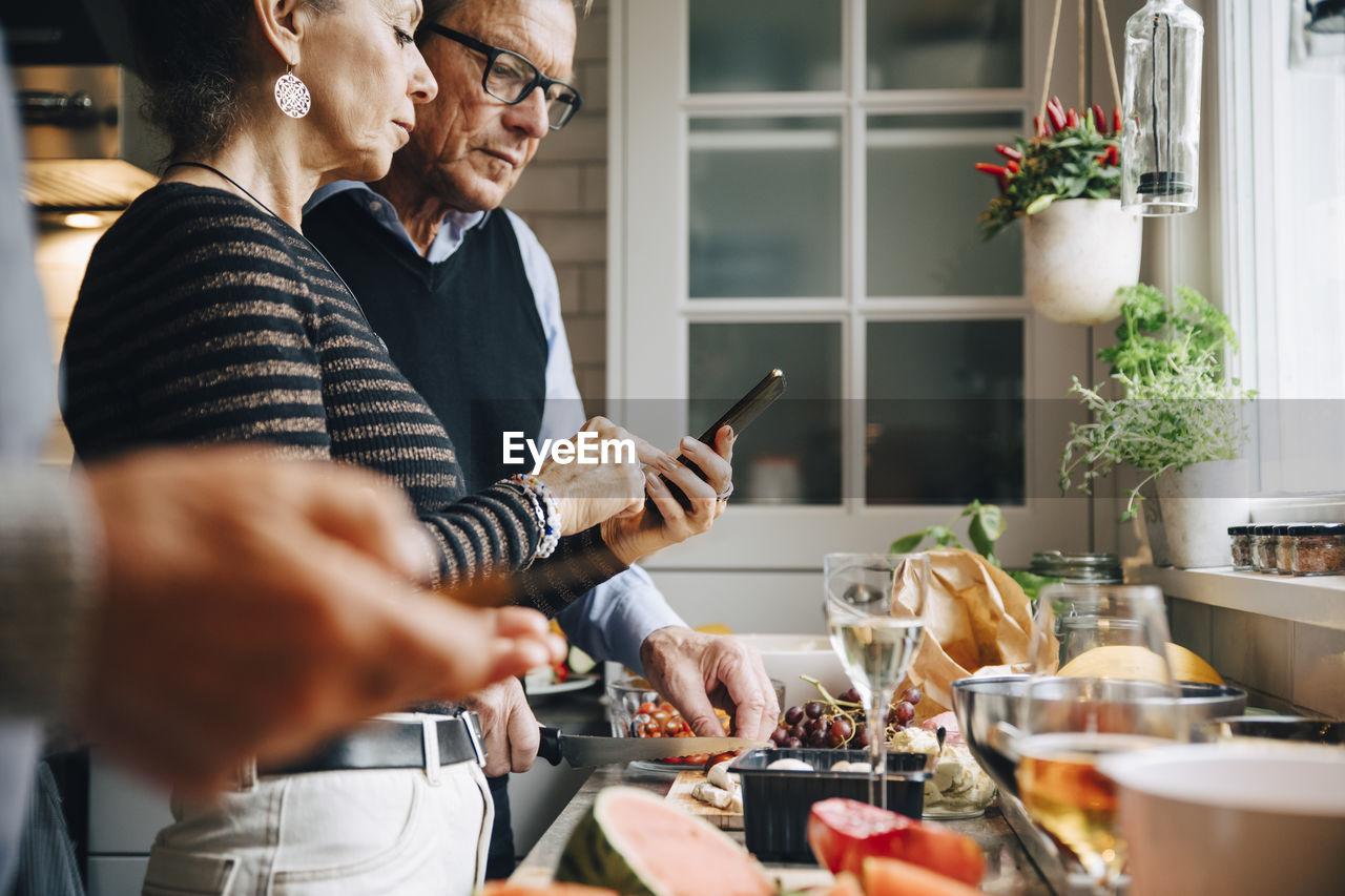 Senior woman showing smart phone to man while preparing dinner in kitchen