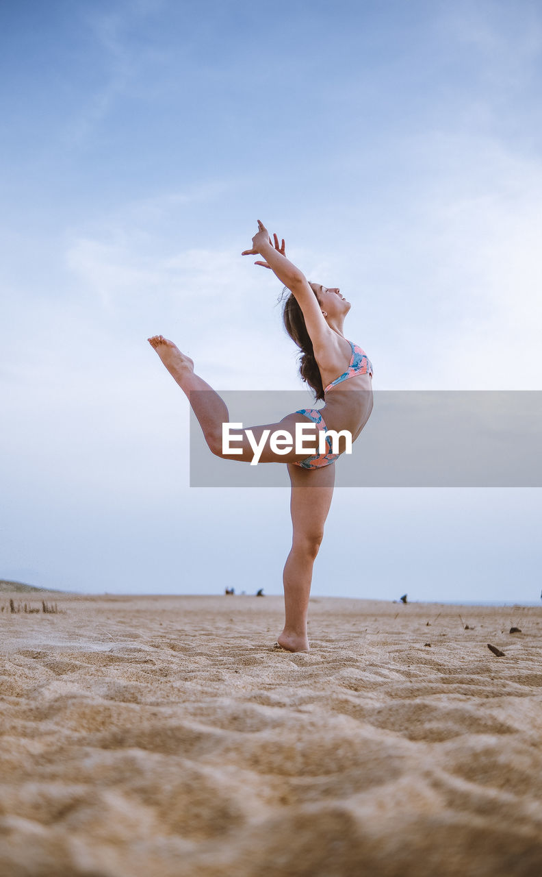 Full length of woman jumping at beach against sky