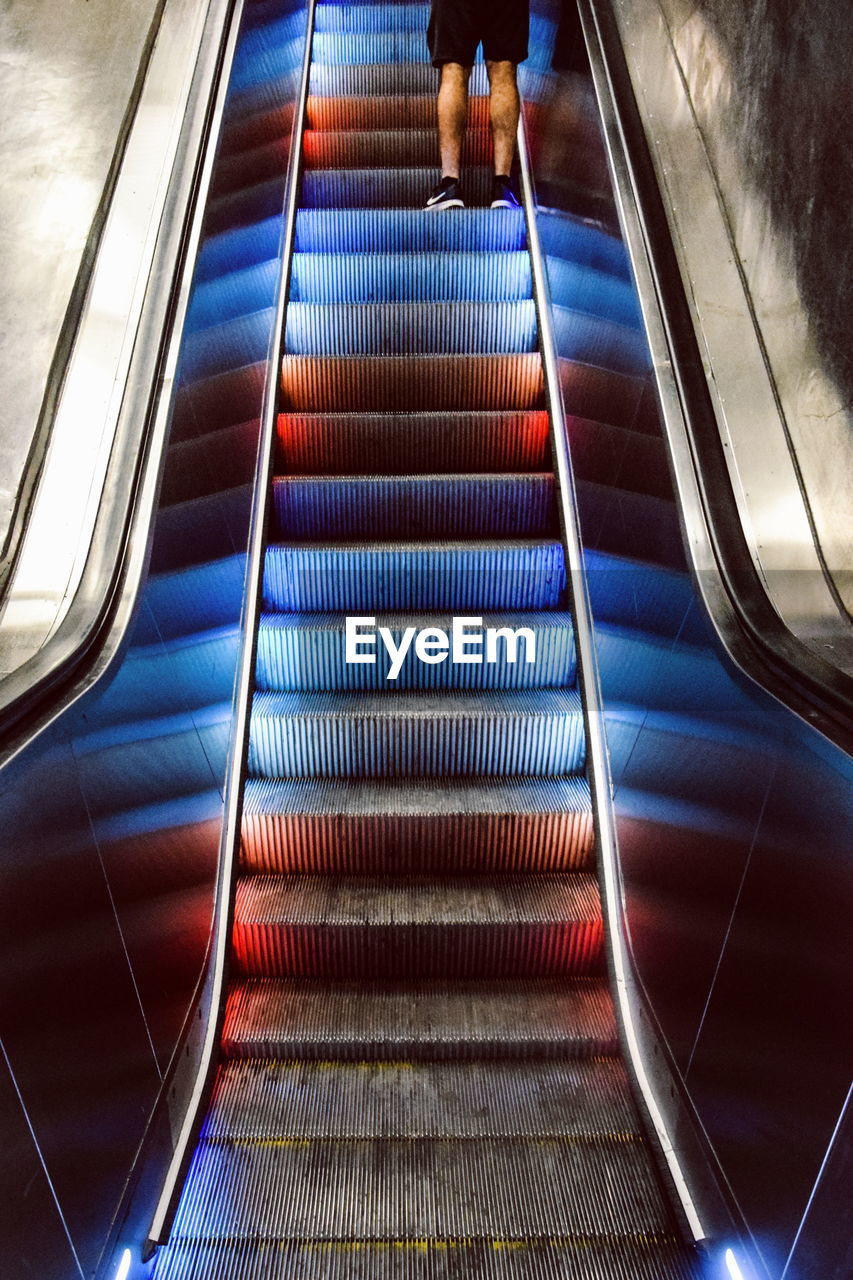 Low section of man standing on illuminated escalator