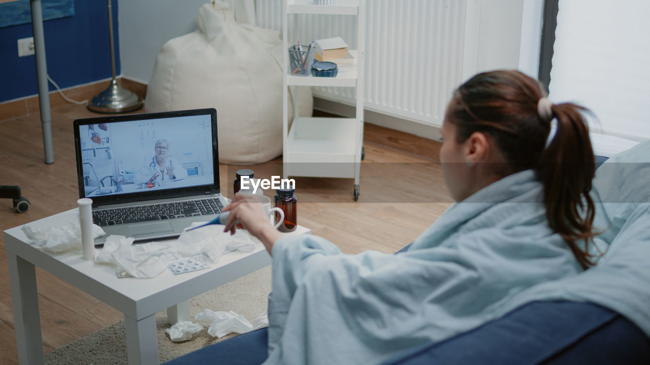 Rear view of woman using laptop at home