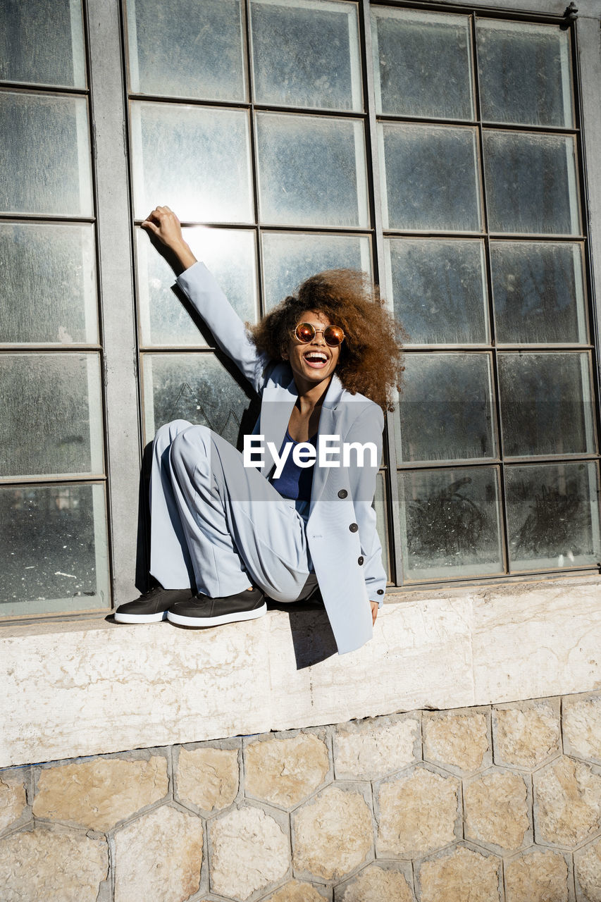 Cheerful young woman sitting while balancing on window sill