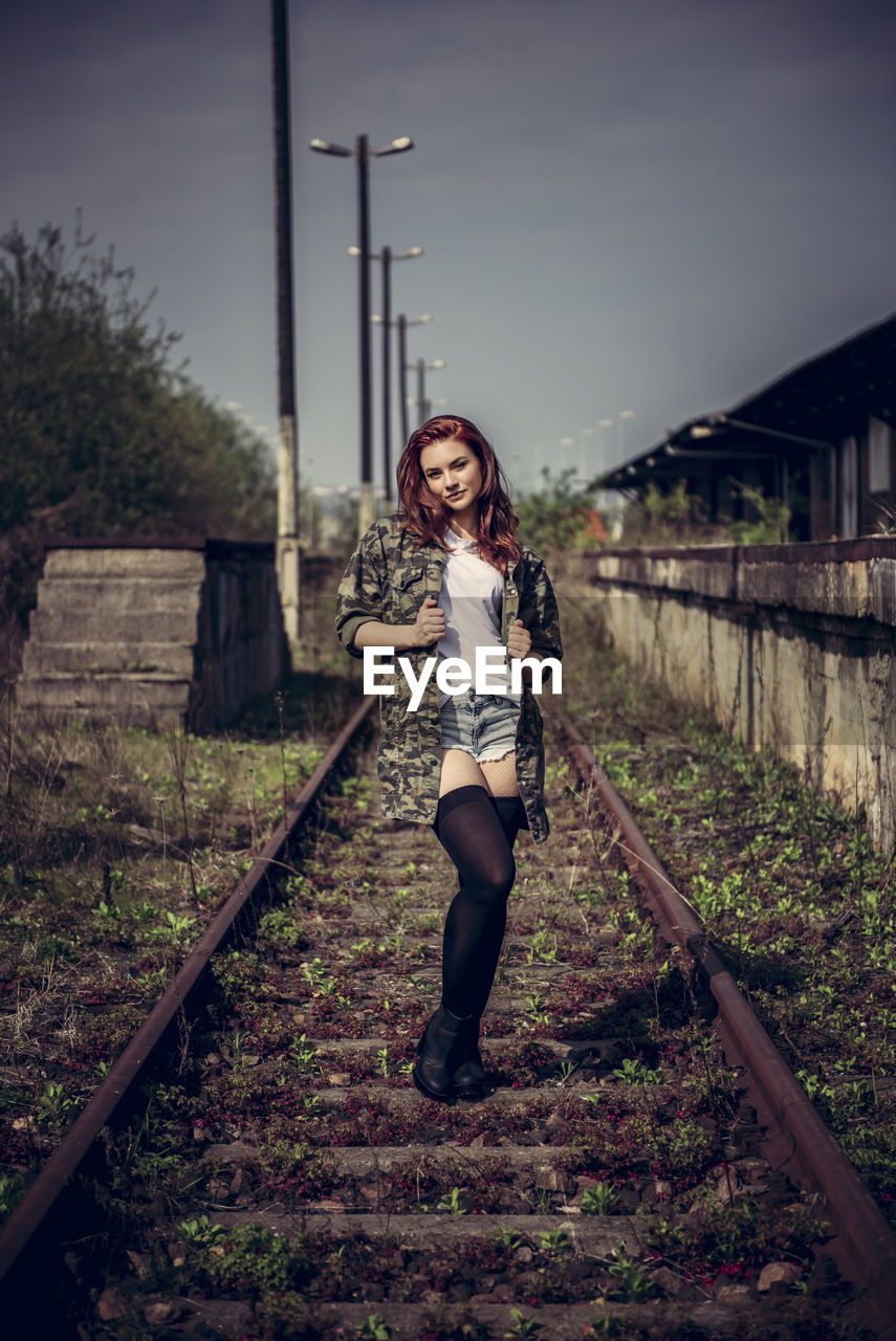 Full length portrait of woman standing on railroad track against sky