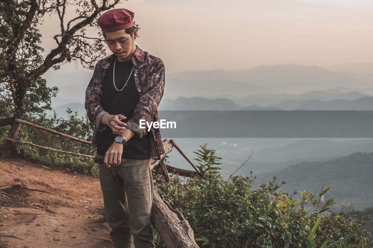 Young man standing on mountain against sky